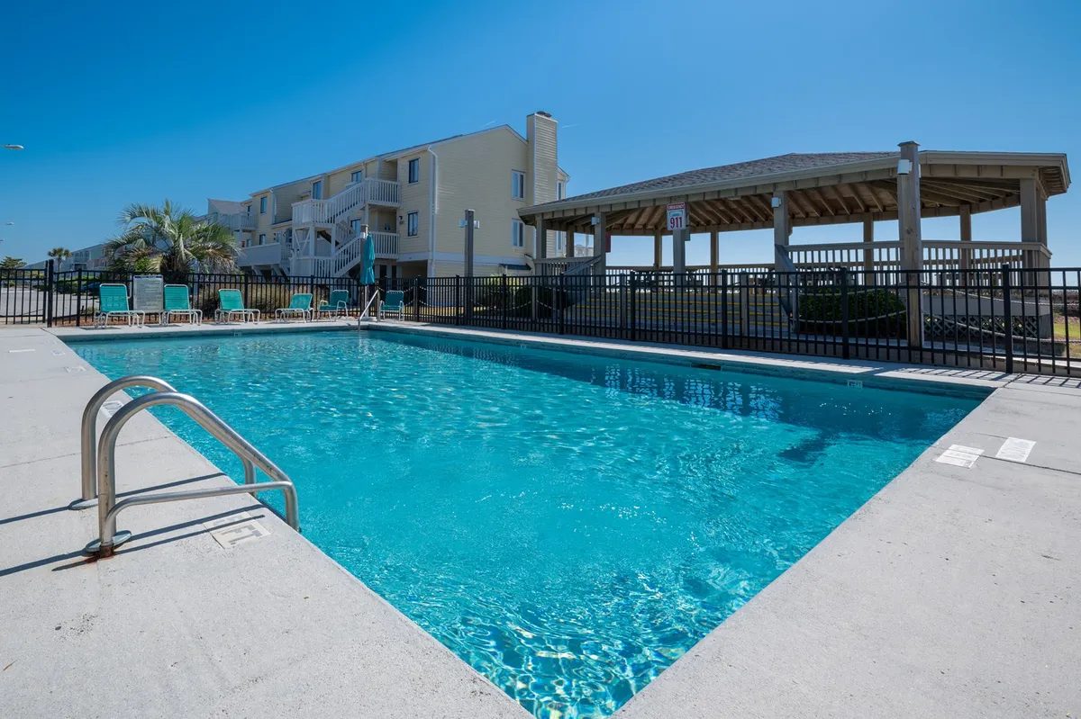 A sparkling swimming pool surrounded by comfortable lounge chairs and a gazebo, all set against a backdrop of sunshine and open sky. The scene radiates relaxation and the opportunity for leisurely swims or poolside lounging at the resort.