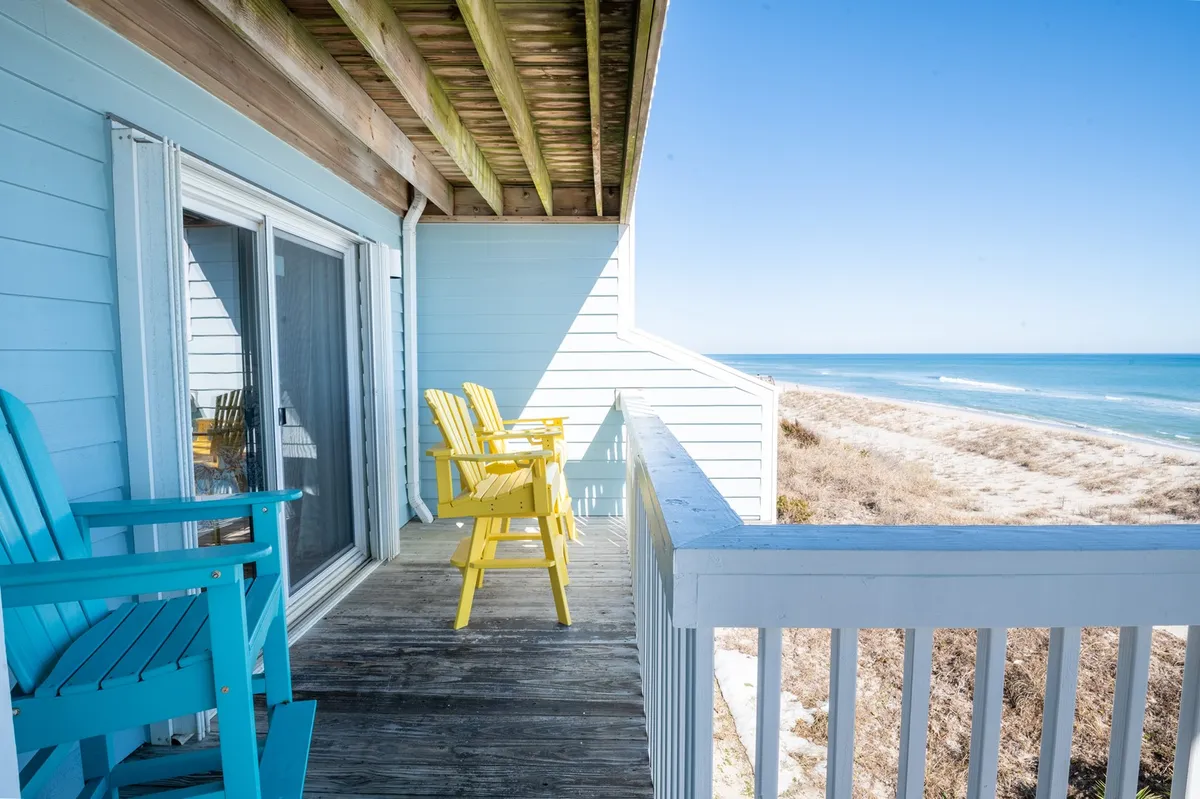 A tranquil wooden deck overlooking the ocean, furnished with colorful chairs arranged to take in the expansive waters and sky. The scene radiates peace, ideal for unwinding, reading, or simply enjoying the fresh seaside breeze at sunrise or sunset.