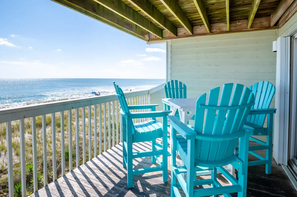 A tranquil private deck overlooking the ocean, furnished with turquoise chairs and framed by a white railing. The space invites relaxation and socializing while taking in spectacular sunrises and the soothing sound of waves.