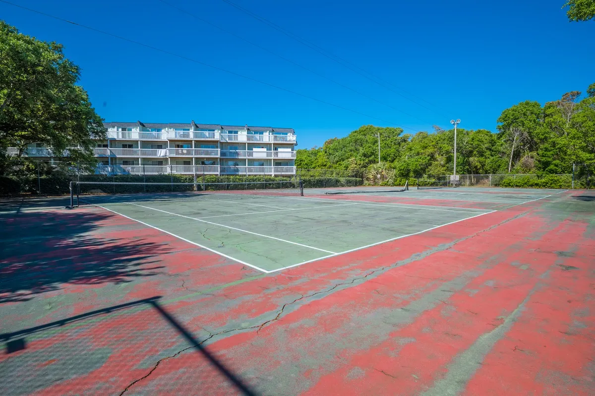 A well-maintained tennis court surrounded by lush greenery and the resort’s apartment building in the background. The scene captures the energy of friendly tennis matches and community events, emphasizing active recreation options.