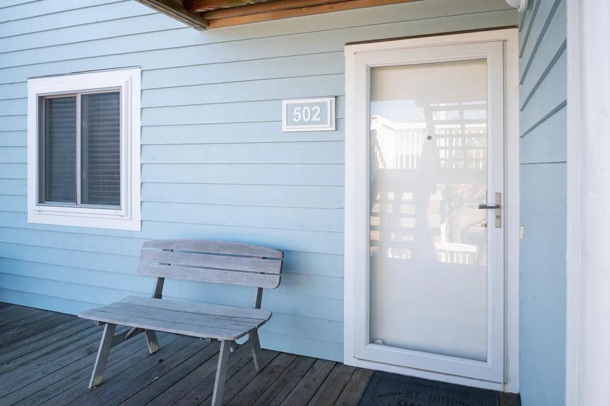 The welcoming front entrance of the property, featuring a bench beside the door and clear house numbers, all set in an inviting exterior space. The mood is friendly and calm, with subtle touches that suggest enjoying the outdoors and easy arrivals.