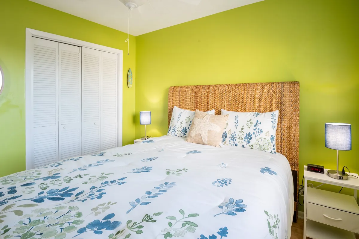 A cozy bedroom featuring a queen bed dressed in floral bedding, a woven headboard, and a nightstand with a lamp, creating a calm and inviting space for relaxation.