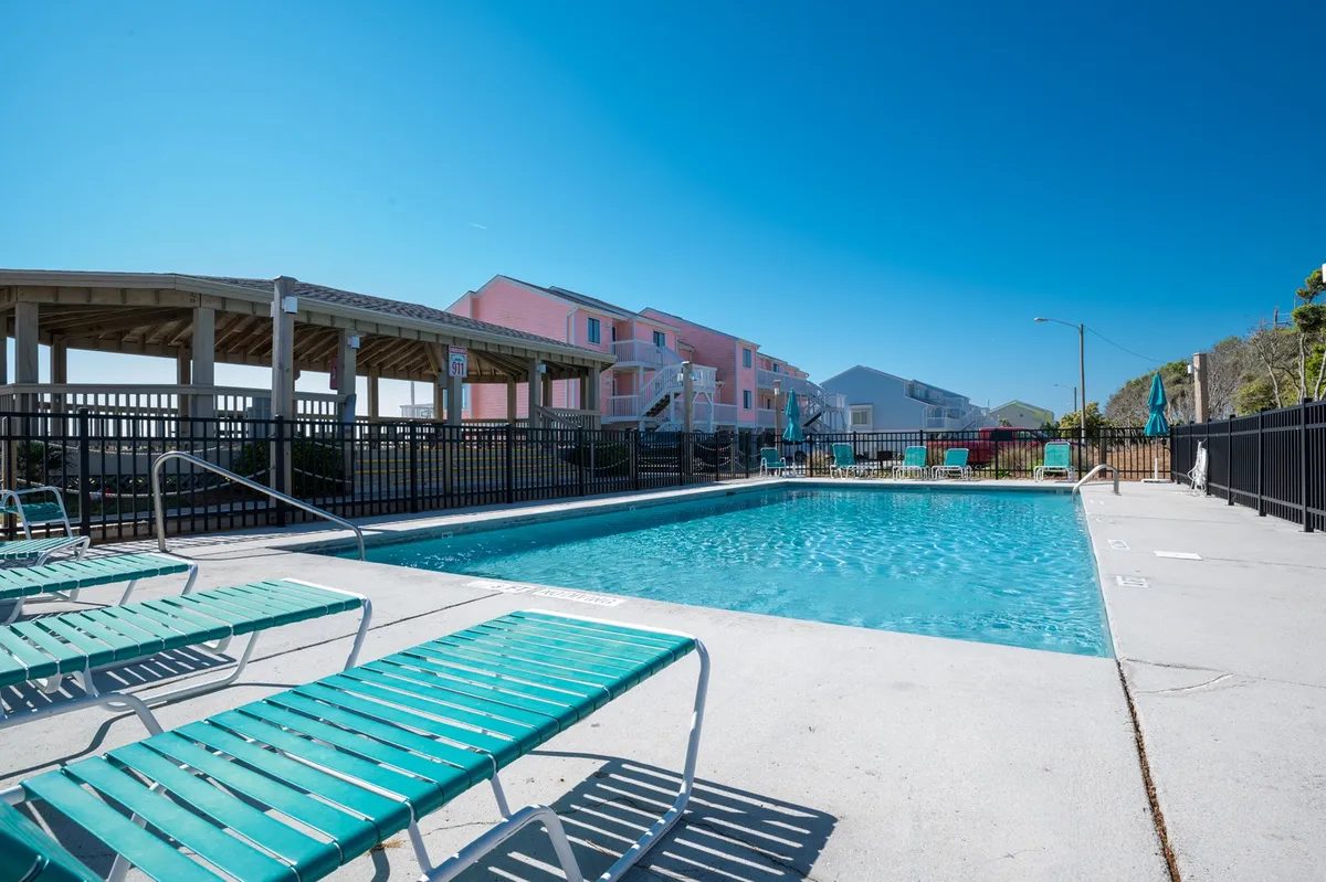 This exterior image shows a swimming pool surrounded by lounge chairs and adjacent buildings. The scene is lively yet relaxed, capturing the essence of poolside fun, sunbathing, and opportunities for group socializing after a day at the beach.