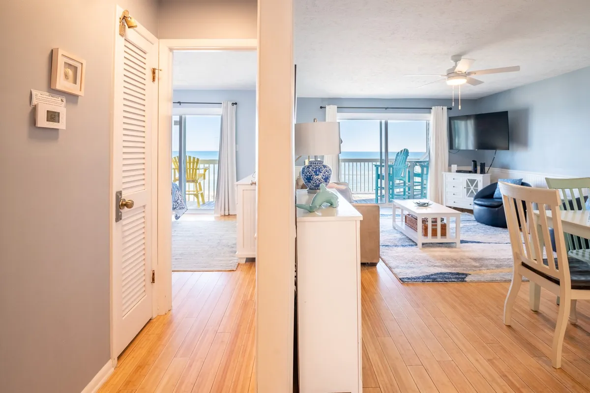 A stylish, tranquil interior space with a clear view through an open doorway to the balcony beyond. Stylish furniture and a decorative lamp set a cozy, inviting mood, while the connection to the outdoor space reinforces the gathering area's open, indoor-outdoor atmosphere.