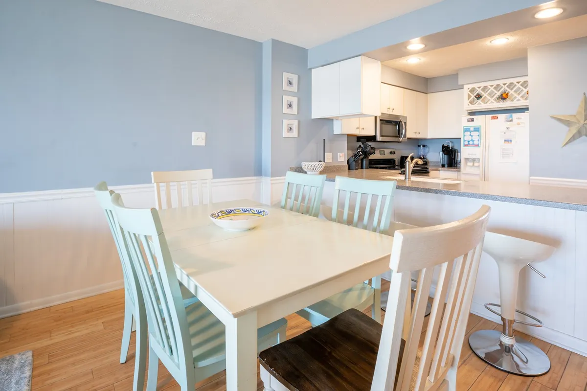 A friendly dining area with a large table set for six, blue accent walls, and a glimpse of the kitchen bar area. The setting feels warm and communal, perfectly suited for both family meals and festive gatherings.