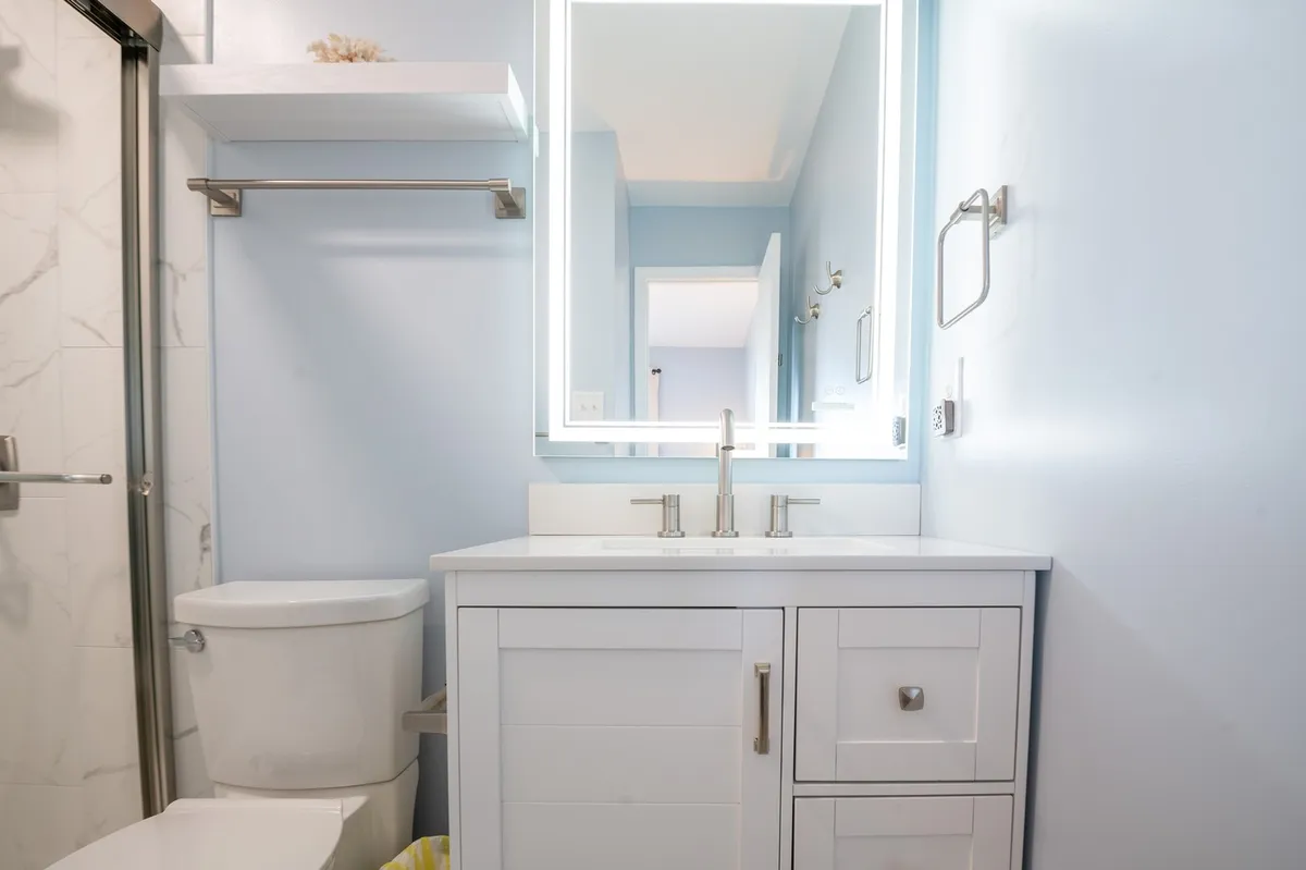 A modern bathroom with a vanity and sink, well-lit mirror, and toilet in a bright, fresh setting. The clean lines and inviting atmosphere suggest comfort and convenience.