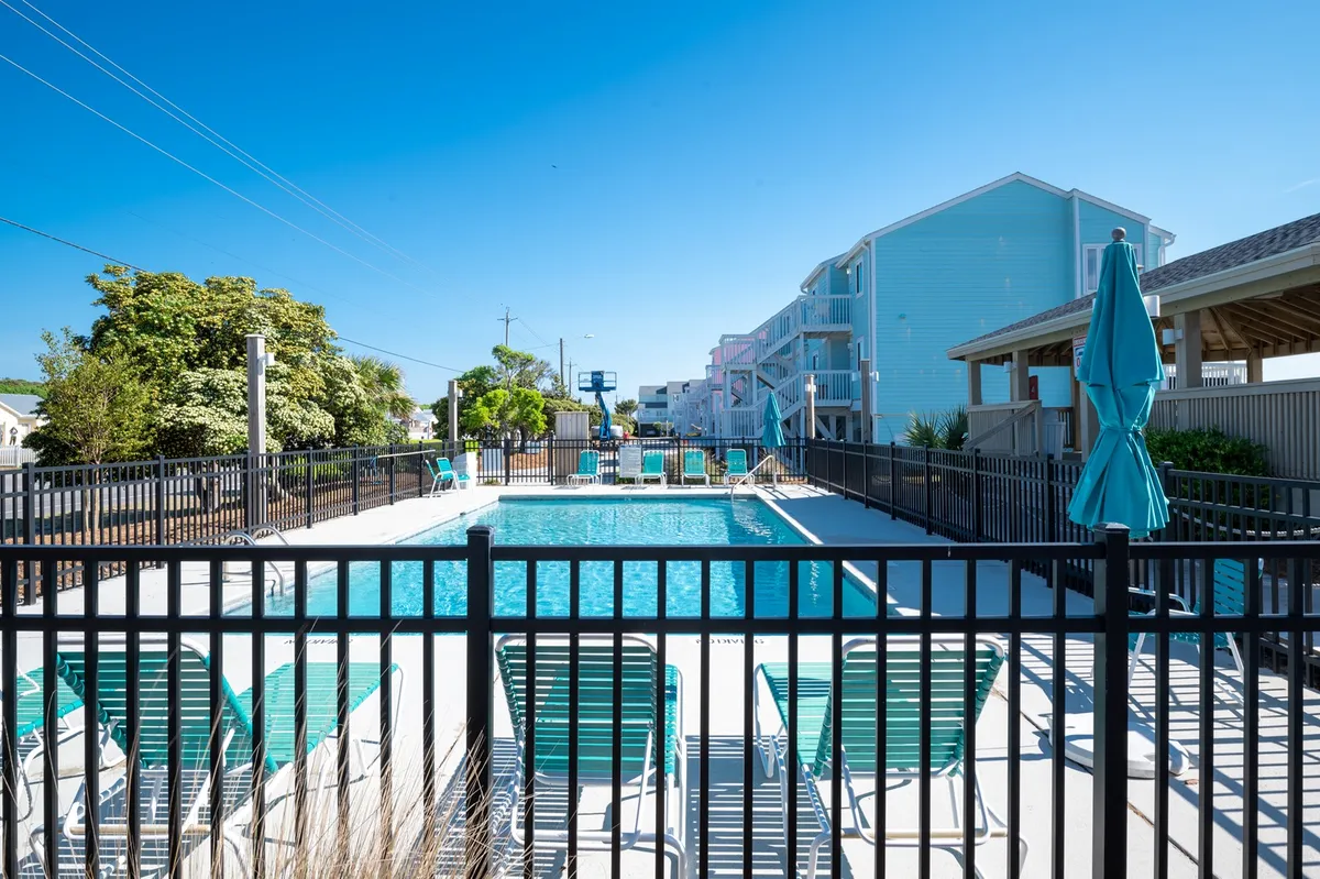 A sparkling swimming pool surrounded by lounge chairs and umbrella shading, inviting guests to swim, sunbathe, or socialize. The area suggests relaxation and fun under the sun, complementing the amenities and summer activities mentioned.