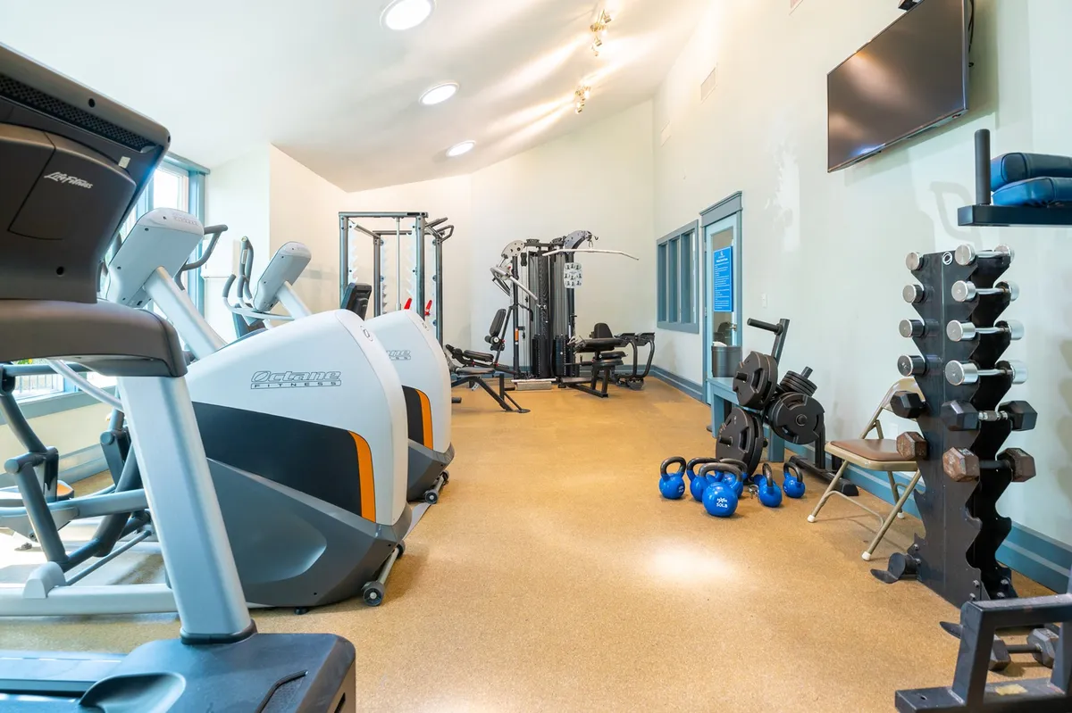 An inviting and modern fitness center interior with treadmills, weight machines, kettlebells, and large windows letting in natural light. The space feels active and energizing, perfect for morning workouts or group fitness activities.